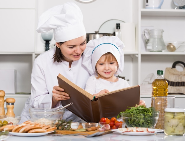 La donna con sua figlia sta guardando insieme la ricetta in libro culinario