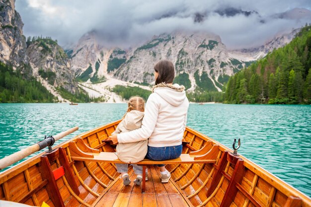 Photo woman with her daughter sitting in big brown boat at lago di braies lake in cloudy day italy