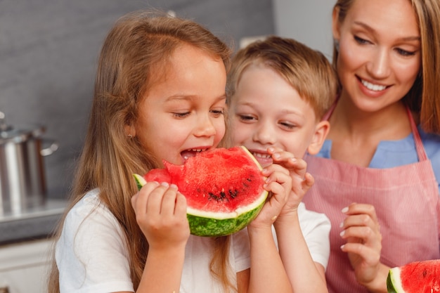 Donna con la figlia e il figlio che mangiano anguria in cucina