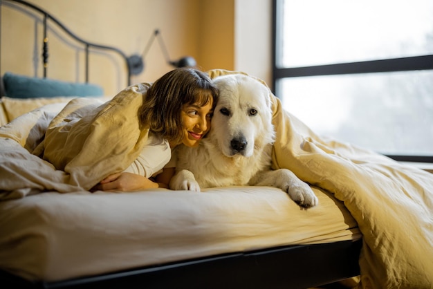 ベッドの毛布の下に犬を連れた女性