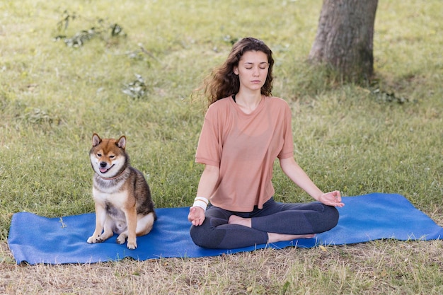 Woman with her dog on a blue yoga mat meditates in a park yoga and meditation for mental and