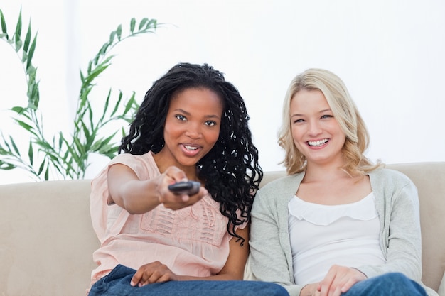 A woman with her friend is pointing a television remote control at the camera