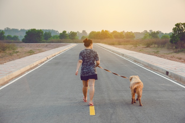 Woman with her golden retriever dog walking on the public road.