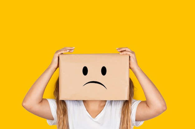 Woman with her head in a box hands on it and sadness gesture on a yellow background with copy space