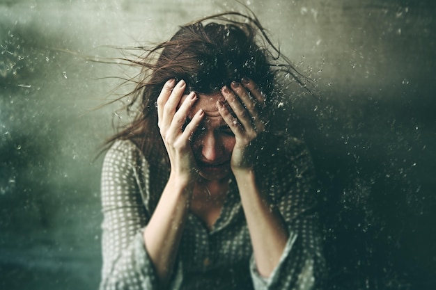 A woman with her head in her hands is sitting on a dirty wall