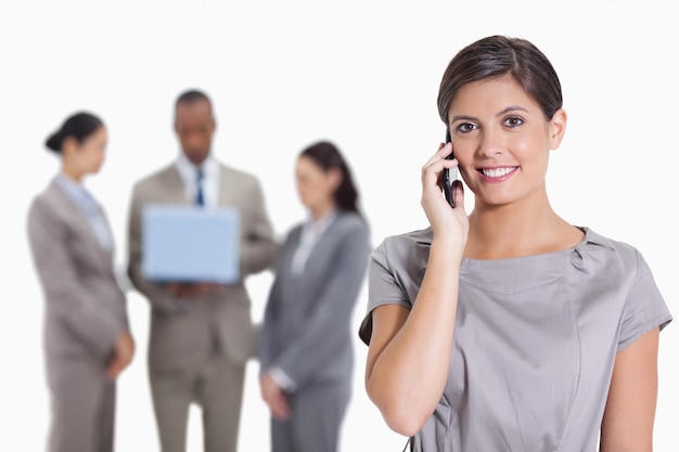 Woman with her head tilted slightly smiling on the phone and coworkers with a laptop