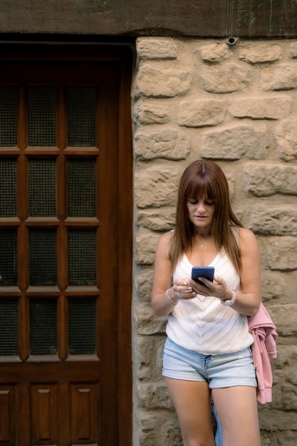 Фото Женщина со своим мобильным телефоном прислонилась к каменной стене