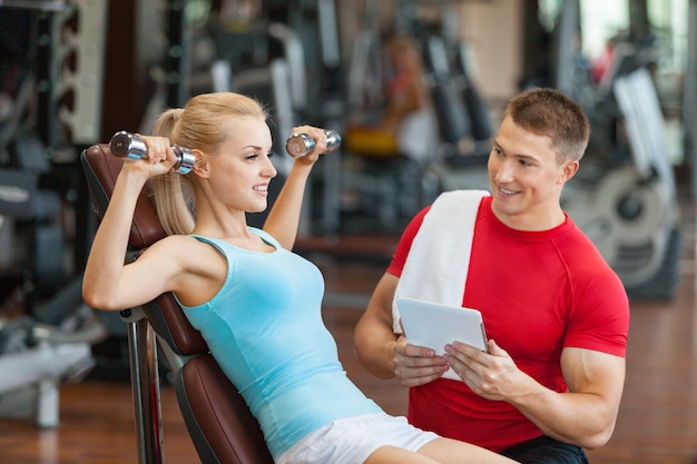 Woman with her personal fitness trainer in the gym exercising with dumbbells