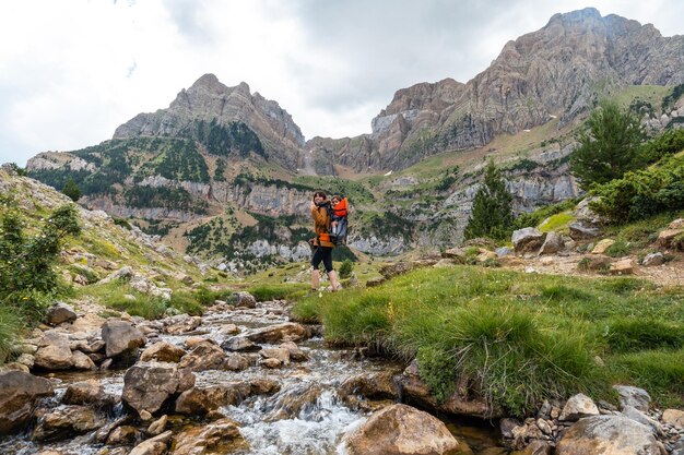 Woman with her son in the backpack walking in the Pyrenees in summer next to a river Tena Valley