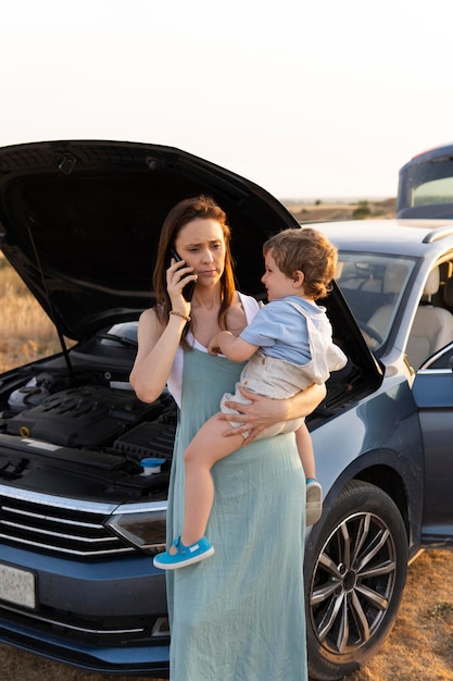 Woman with her threeyearold son with the car broken down\
calling a tow truck or insurance roadside assistance concept