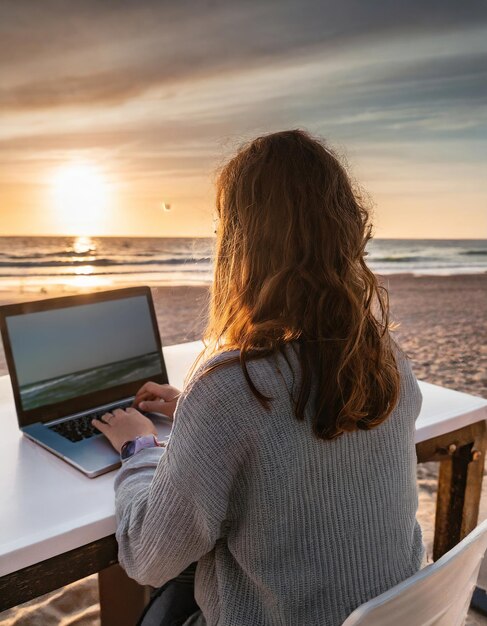 사진 해변에서 일몰을 시청하는 노트북을 사용하는 여성 디지털 유목민의 개념