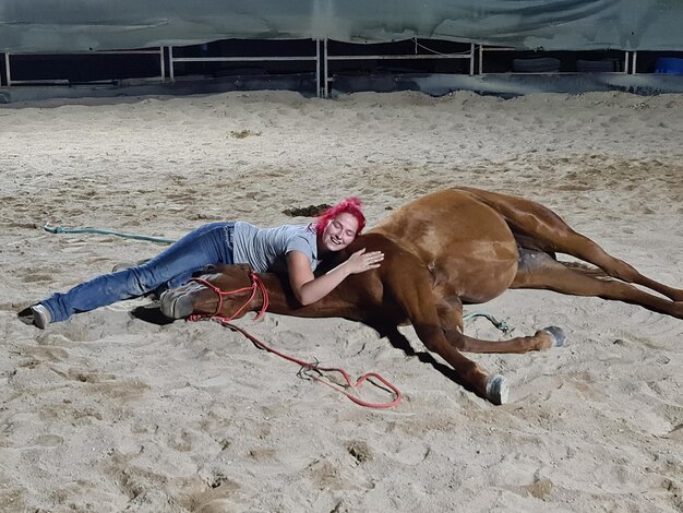 写真 砂の上に横たわっている馬を持つ女性