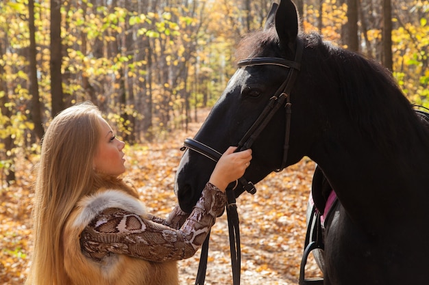 秋の森を散歩する馬を持つ女性