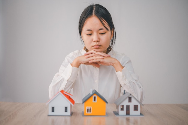 Woman with a house model in front of her is making a decision to buy a new home concept of buying a house