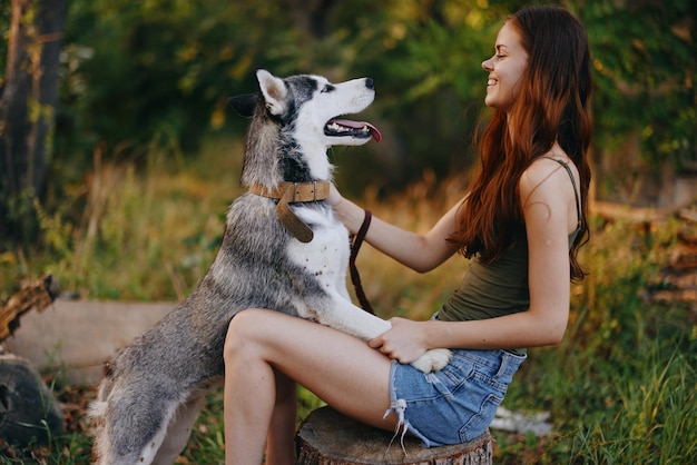 A woman with a husky breed dog smiles and affectionately strokes her beloved dog while walking in nature in the park in autumn against the backdrop of sunset High quality photo