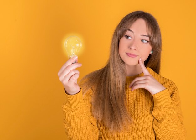 Photo woman with an idea, holding a light bulb on yellow background