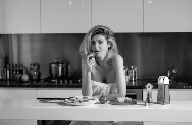Woman with ingredients for pizza cheese sausage and tomato Young woman eating breakfast Sexy slim woman at home in morning Beautiful sensual female housewife in towel with bare shoulders