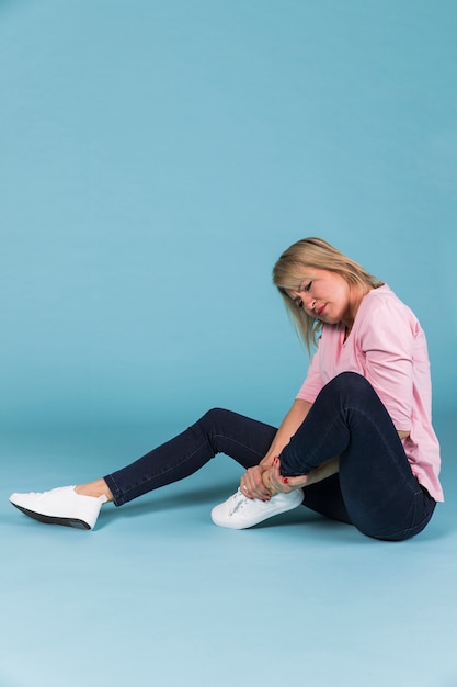 Woman with injured foot sitting on blue background