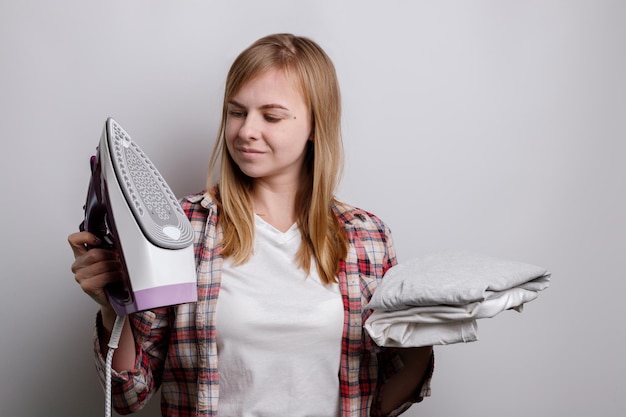 A woman with an iron and underwear that needs to be ironed on a gray background