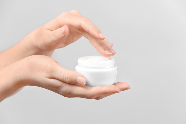 Woman with jar of body cream on light background