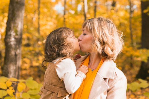 Женщина с ребенком девочка на открытом воздухе осенью ребенок целует мама день матери праздник и осенняя концепция