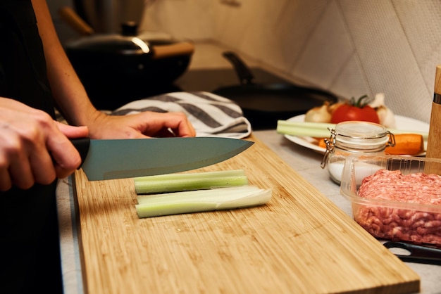 Woman with knife cuts fresh celery slices for cooking