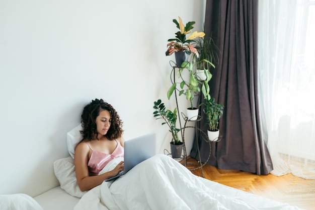 Woman with laptop in bed freelancer internet shopping