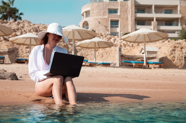 A woman with a laptop on a sand is resting and working as a freelancer