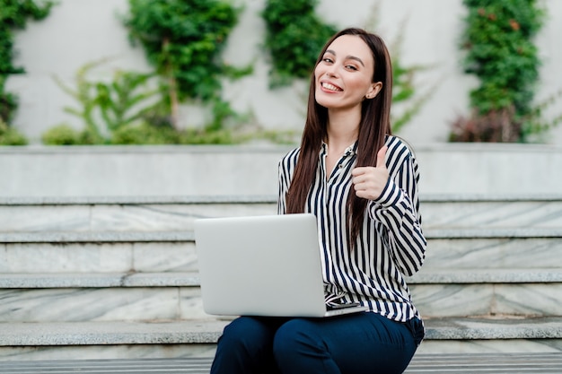 La donna con il computer portatile mostra i pollici in su