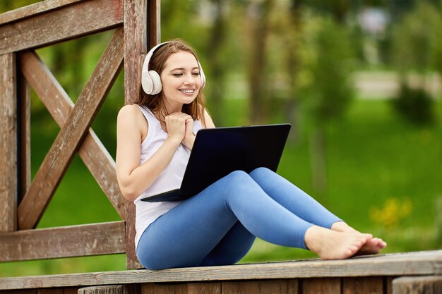 Woman with laptop sits outdoors in cordless headphones