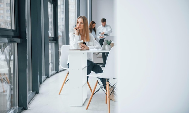 Donna con laptop seduto di fronte a un gruppo di giovani team di successo che lavorano e comunicano insieme al chiuso in ufficio