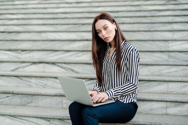 Woman with laptop sitting on stairs in the city