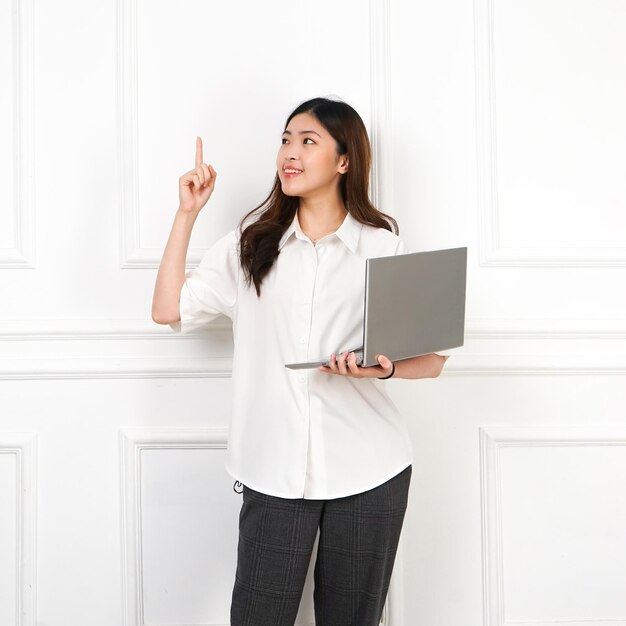 A woman with a laptop and a white shirt pointing up.