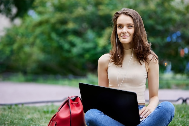 Woman with laptop  years old sits on lawn in city park