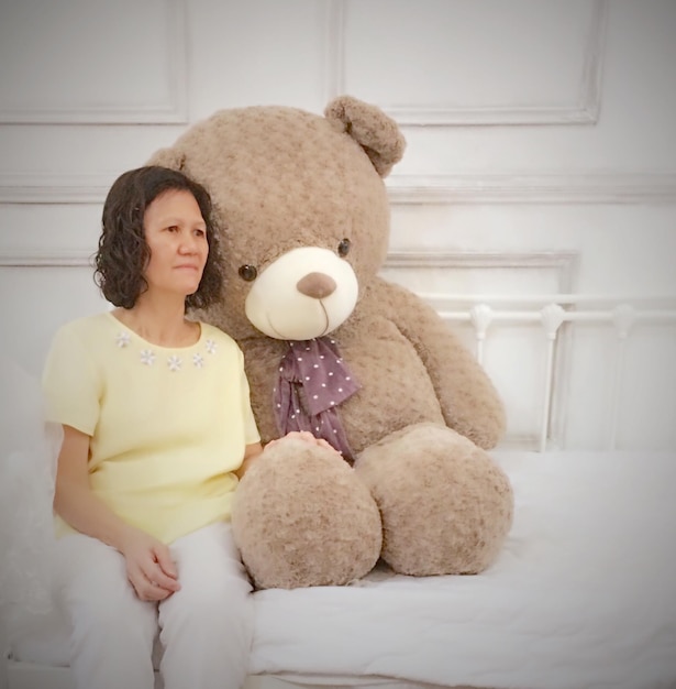 Photo woman with large teddy bear sitting on bed at home