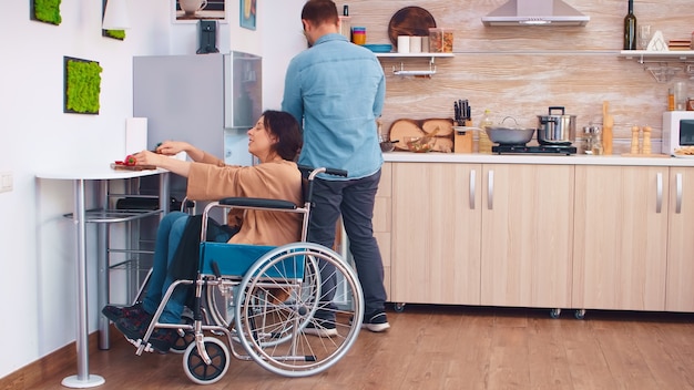 Woman with legs paralysis in wheelchair cutting red pepper on slicing board. Woman with paralysis handicap disability handicapped difficulties helping in the kitchen