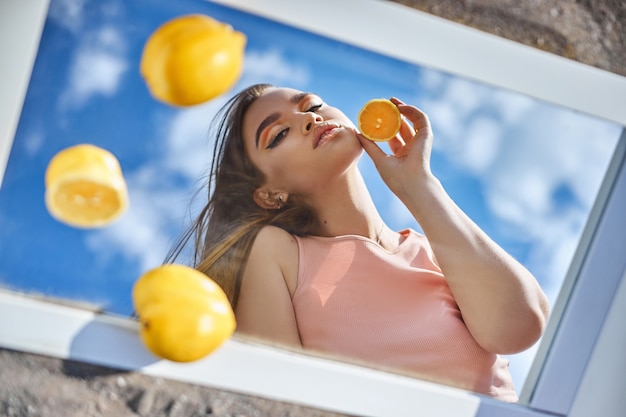 Женщина с лимоном в руках, питание красоты кожи витамином С. Натуральная косметика для ухода за кожей лица. Солнечный день голубое небо