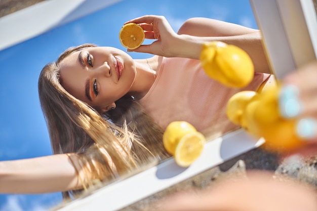 Donna con un limone in mano, nutrizione della pelle di bellezza con vitamina c. cosmetici naturali per la cura della pelle del viso. giornata di sole cielo blu