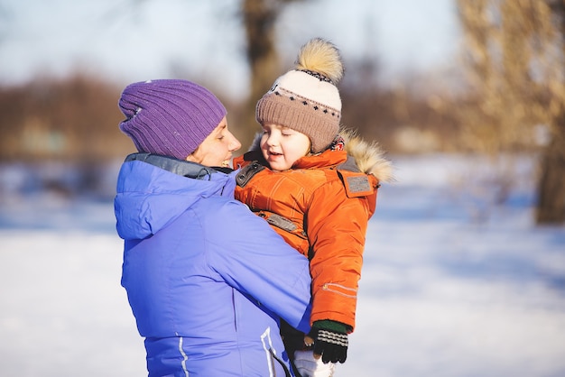 Woman with little son playing in the park in winter on snow.