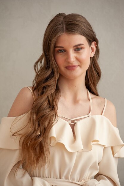 A woman with long brown hair and a beige dress with a gold chain on the neck.