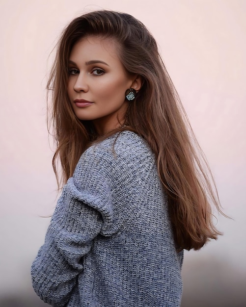 A woman with long brown hair stands in front of a pink background.