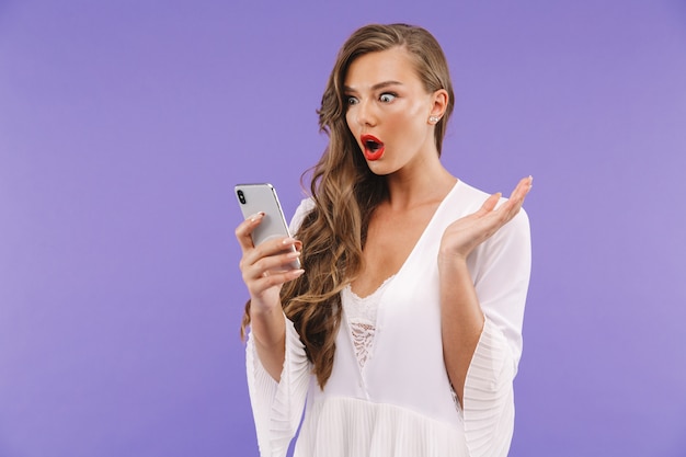 Woman with long curly hairstyle wearing dress holding and looking at mobile phone,