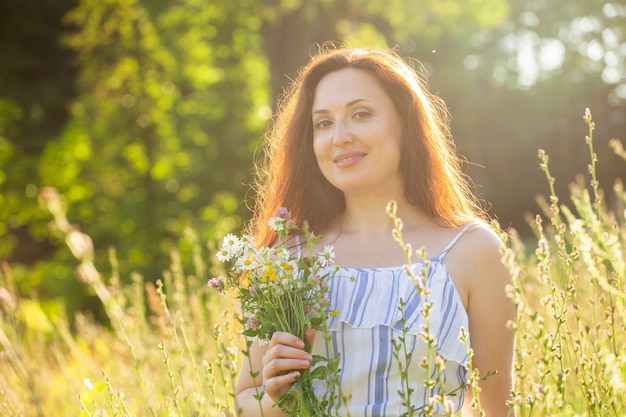 Woman with long hair in dress walking through the summer forest on a sunny day