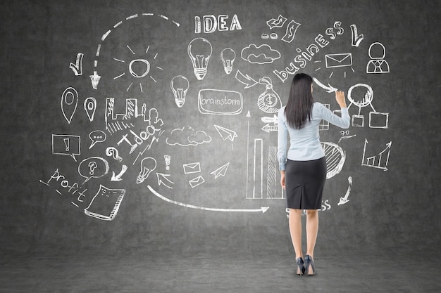 Woman with long hair is drawing startup sketch on blackboard