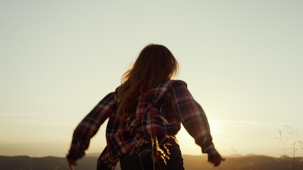 A woman with long hair is standing in front of a window with the sun behind her.