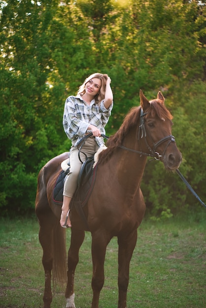 Woman with long hair posing with a brown horse in a forest in a sunny meadow