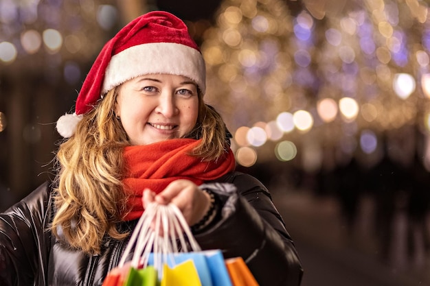 Photo a woman with long hair and a santa hat  with purchases in colorful paper bags new years shopping