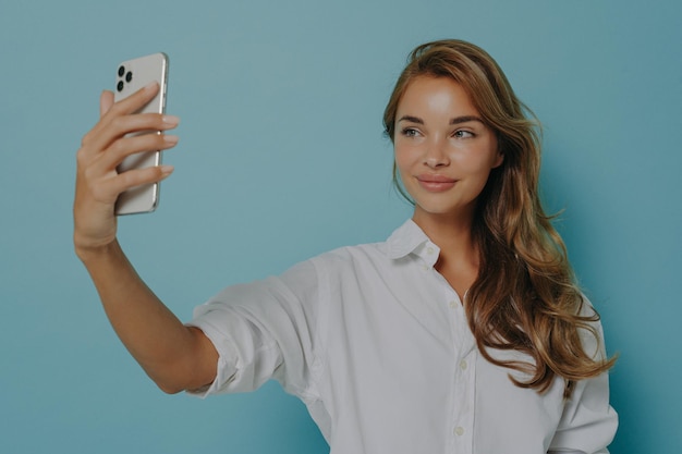 Woman with long hair takes selfie via modern smartphone takes photo of herself makes video call