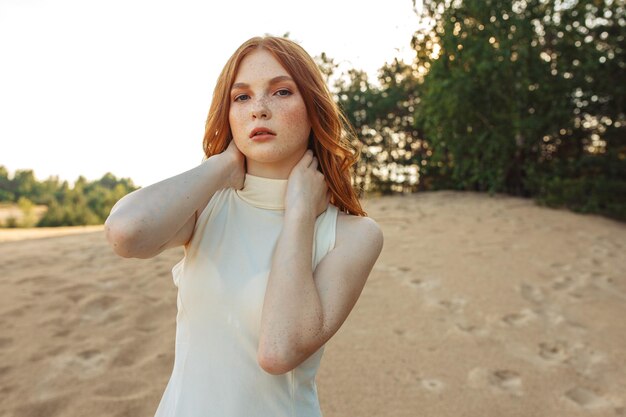 woman with long red hair and freckles looking at camera while touching neck