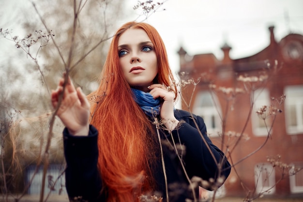 Woman with long red hair walks in autumn on street. Mysterious dreamy look and image of girl. Redhead woman walking